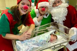 Cztery postacie w strojach świątecznych przy noworodku.