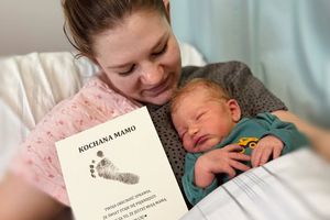 Matka trzyma noworodka z kartką.