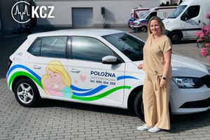 Polożna obok auta z logo.