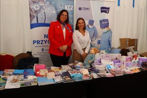 Kobiety przy stoisku z materiałami promocyjnymi.