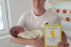 Mężczyzna trzyma noworodka i certyfikat.